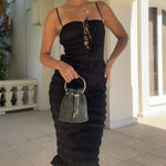 A model holding a small silver crystal drawstring ring top handle bag outside against a white wall. 