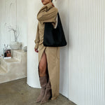 A model wearing a black large recycled vegan leather shoulder bag against a white wall. 