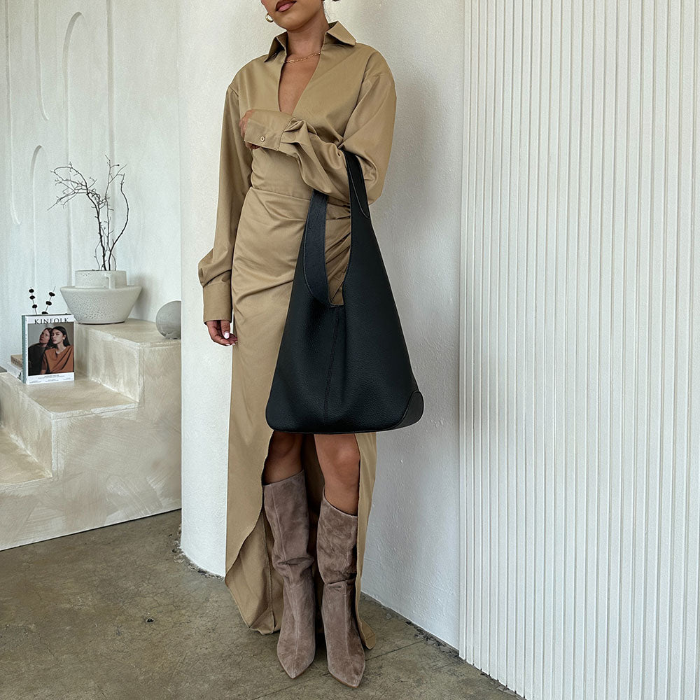 A model wearing a large black recycled began leather shoulder bag against a white wall.