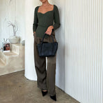 A model wearing a black woven wide strap vegan leather tote bag against a white wall. 