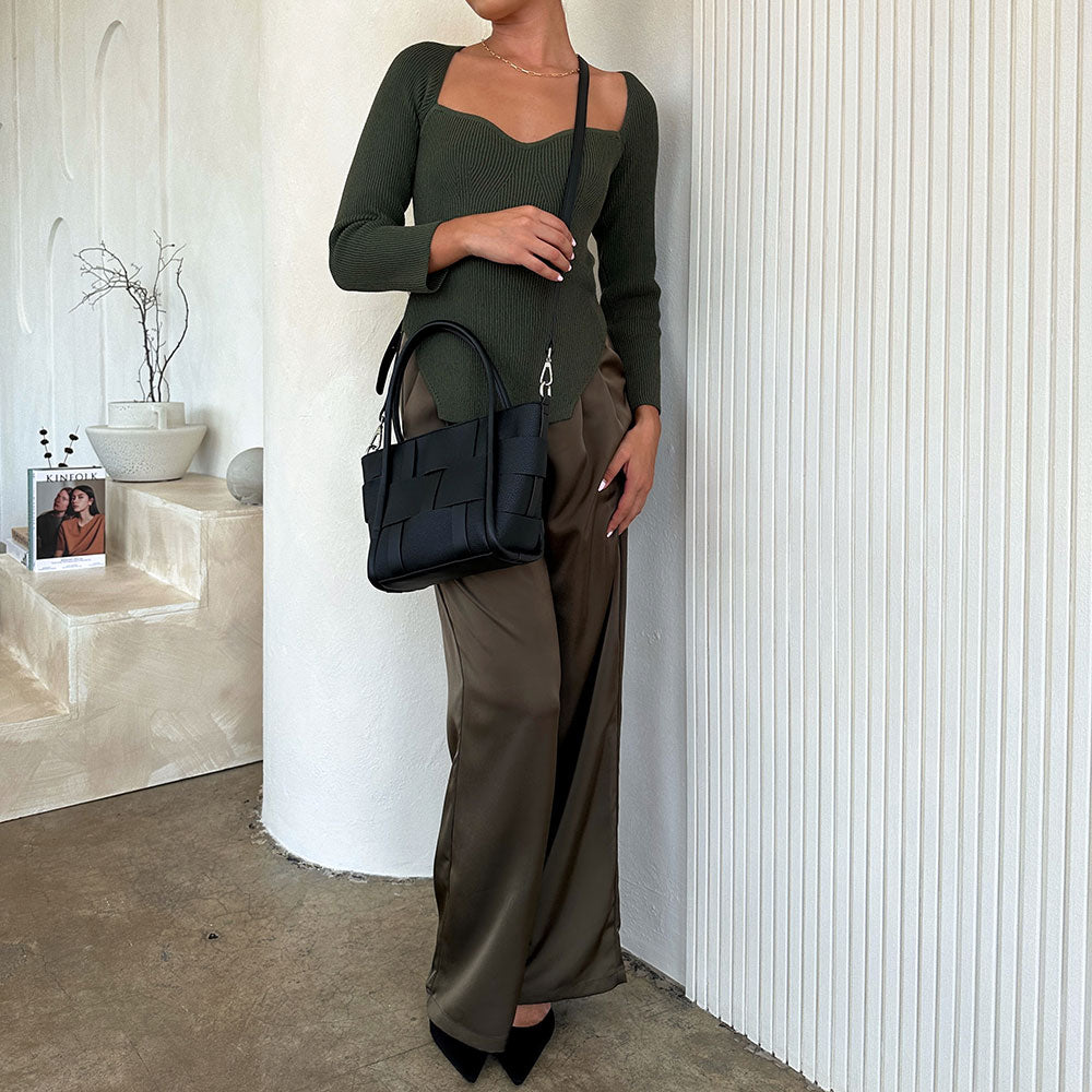 A model wearing a small woven wide strap vegan leather tote bag against a white wall. 