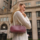 Woman carrying a burgundy handbag in an urban setting.