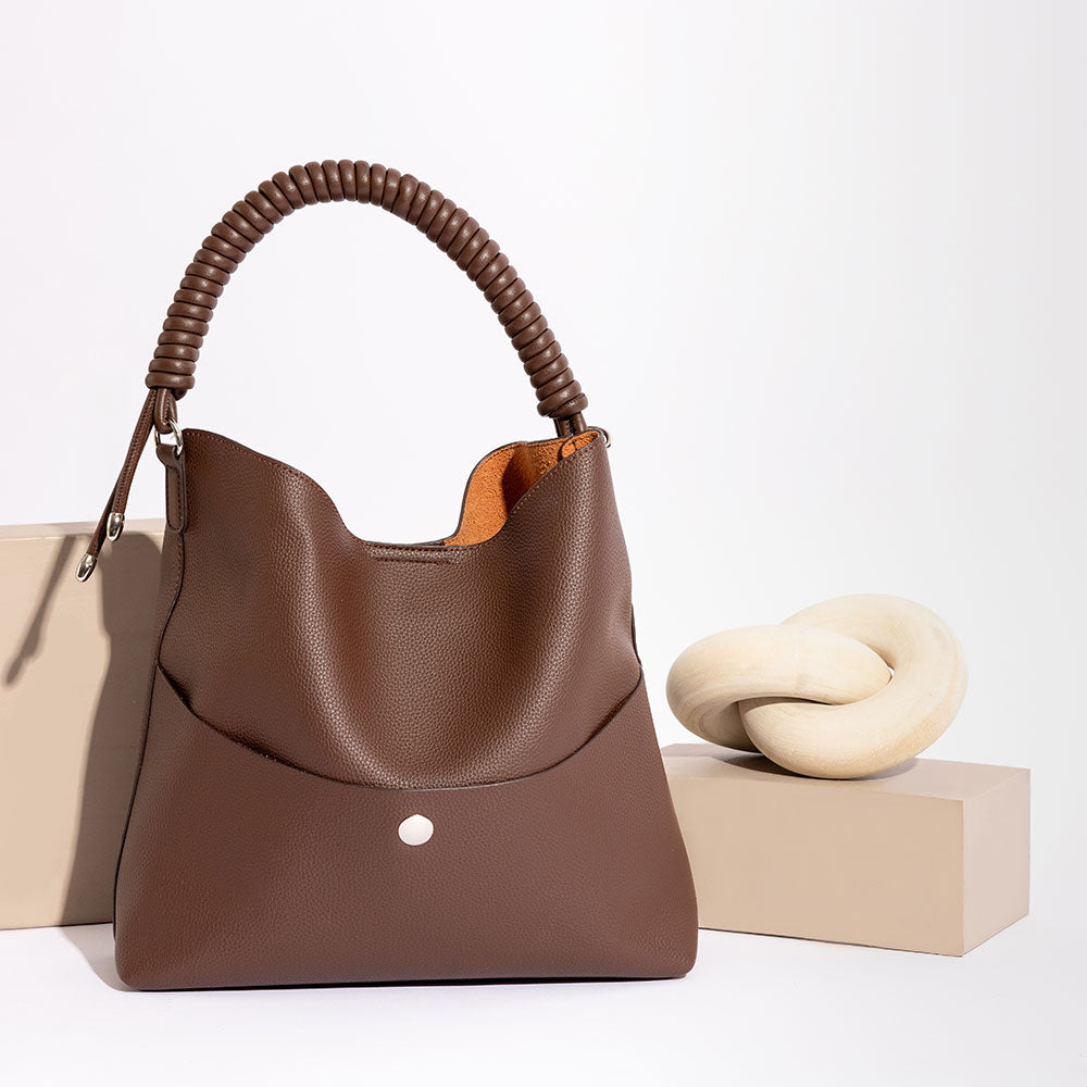 A still image of a pebble vegan leather tote bag with a spiral handle against a wood prop.