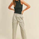 A model wearing a beige high rise cargo pant against a tan wall. 