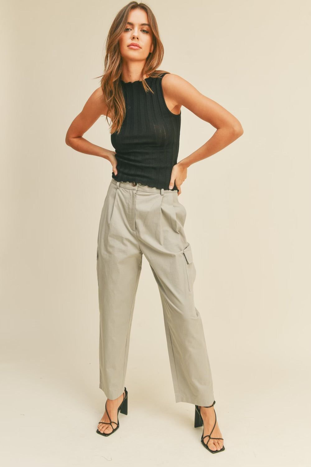 A model wearing a beige high rise cargo pant against a tan wall. 