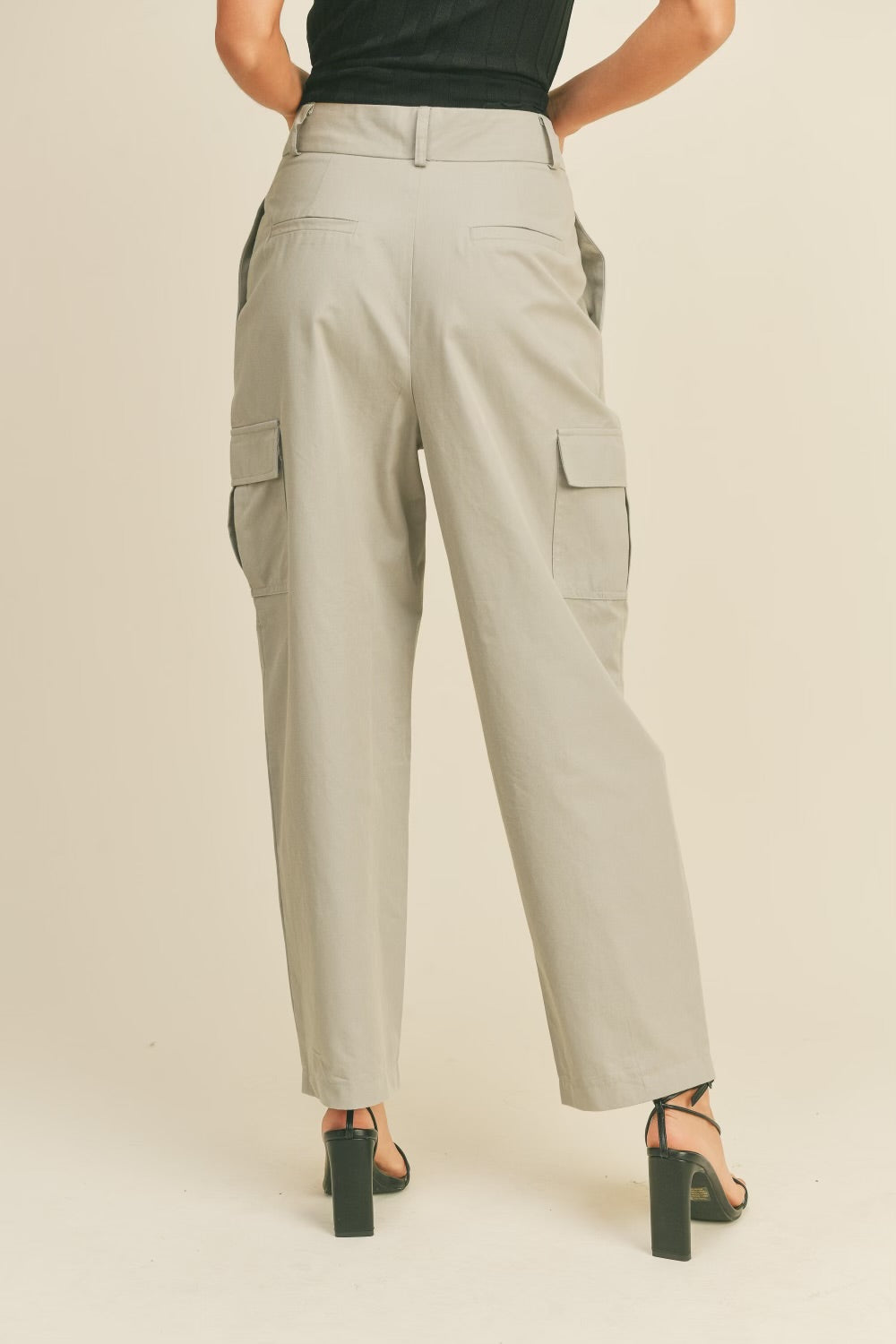 A model wearing a beige high rise cargo pants backside view against a tan wall. 