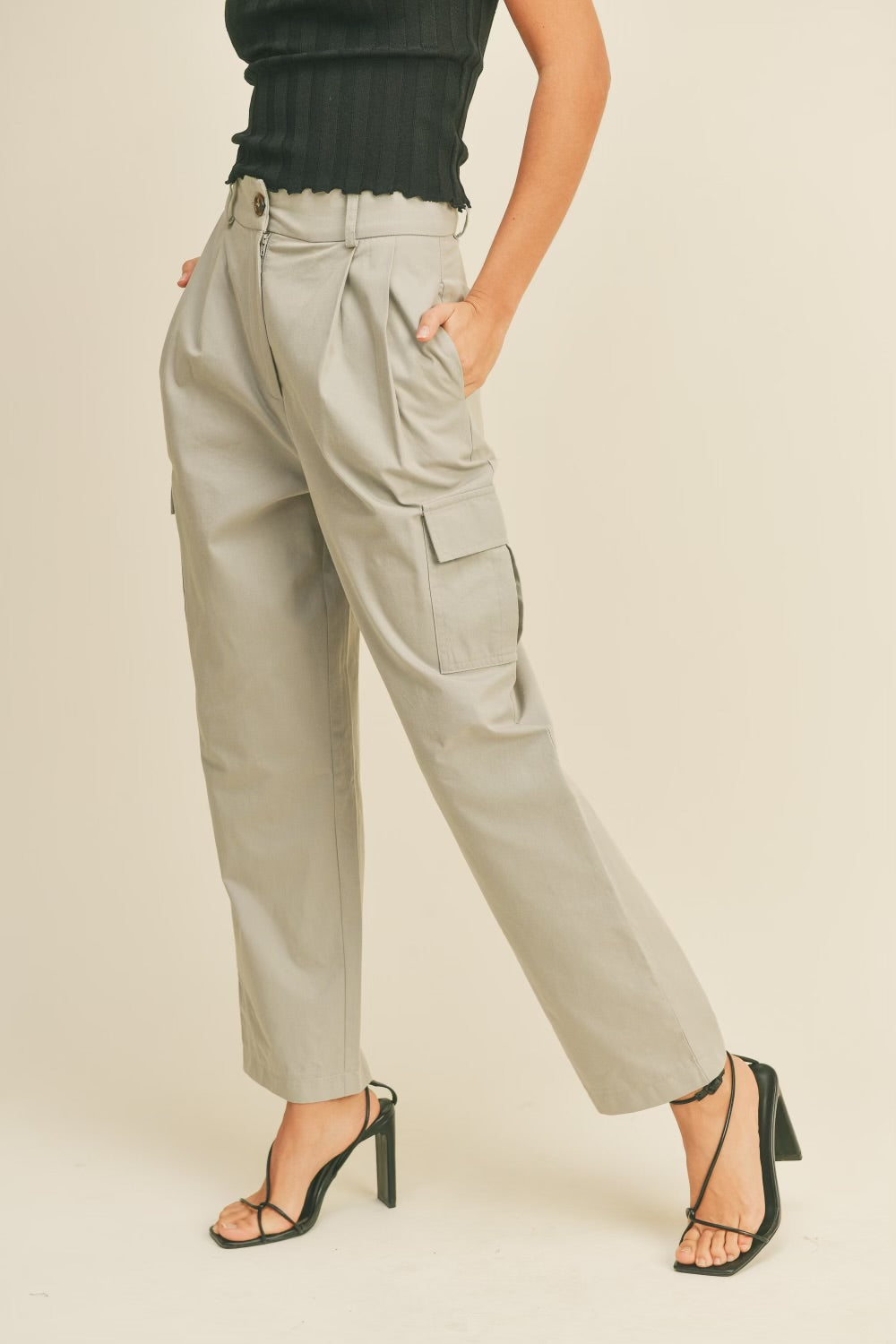 A model wearing a beige high rise cargo pant against a tan wall.
