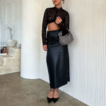 A model wearing a small crystal encrusted top handle bag with a knot against a white wall. 