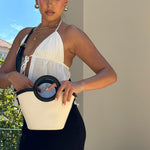 A model wearing a small canvas and vegan leather crossbody bag with a circle handle against a wall outside. 