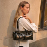 Woman holding an olive leather handbag against a beige wall.