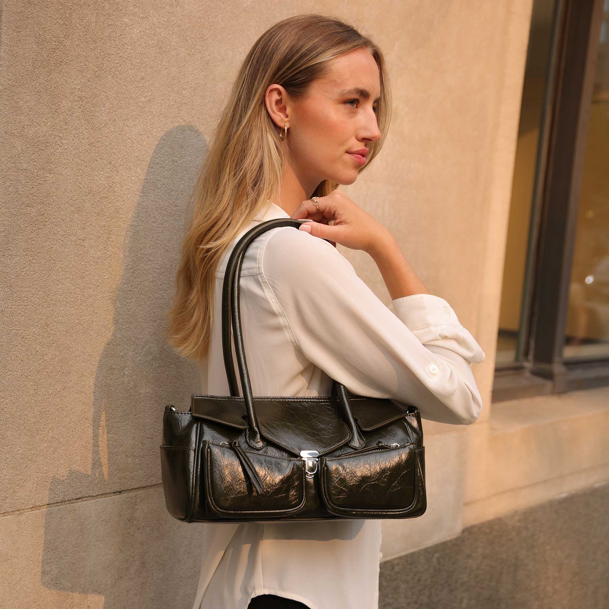 Woman holding an olive leather handbag against a beige wall.