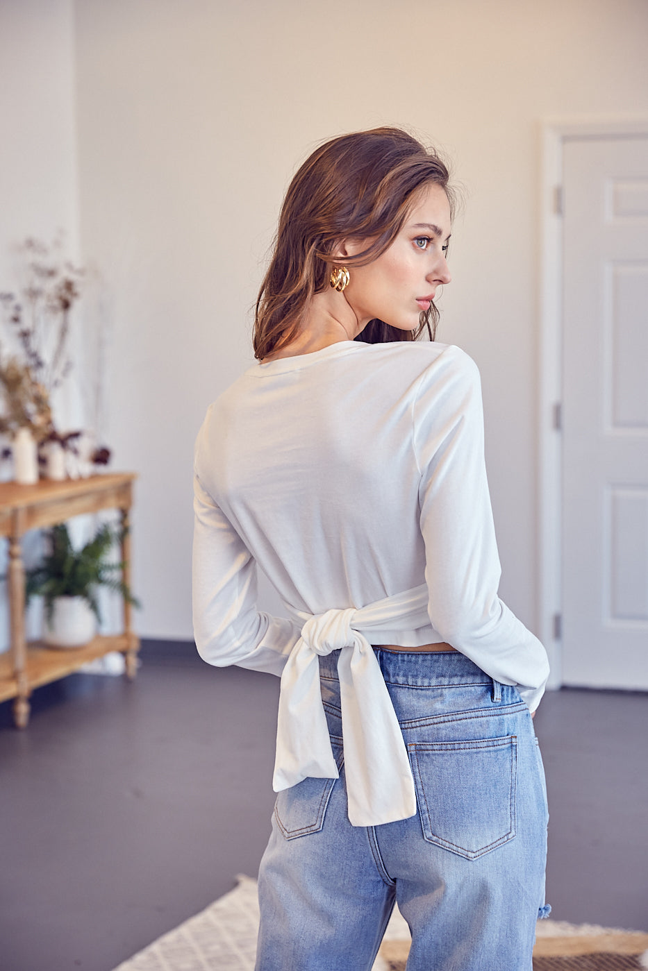 A model wearing a white front cross tie top backside view against a white wall. 