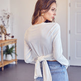 A model wearing a white front cross tie top backside view against a white wall. 