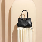 A still image of a hand woven vegan leather crossbody againast a tan wall. 