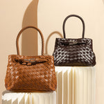A still image of two hand woven vegan leather crossbody bags with curved handles against a tan wall. 