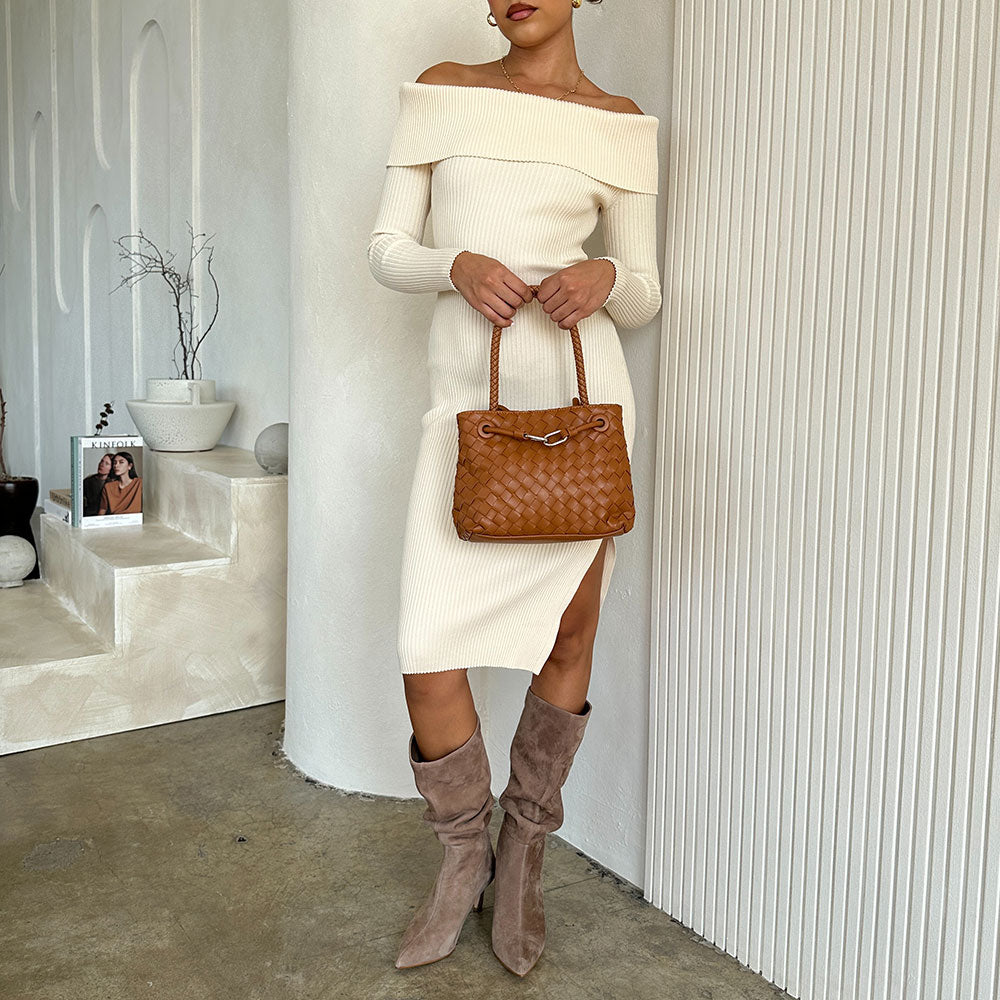 A model wearing a hand woven crossbody bag against a white wall. 