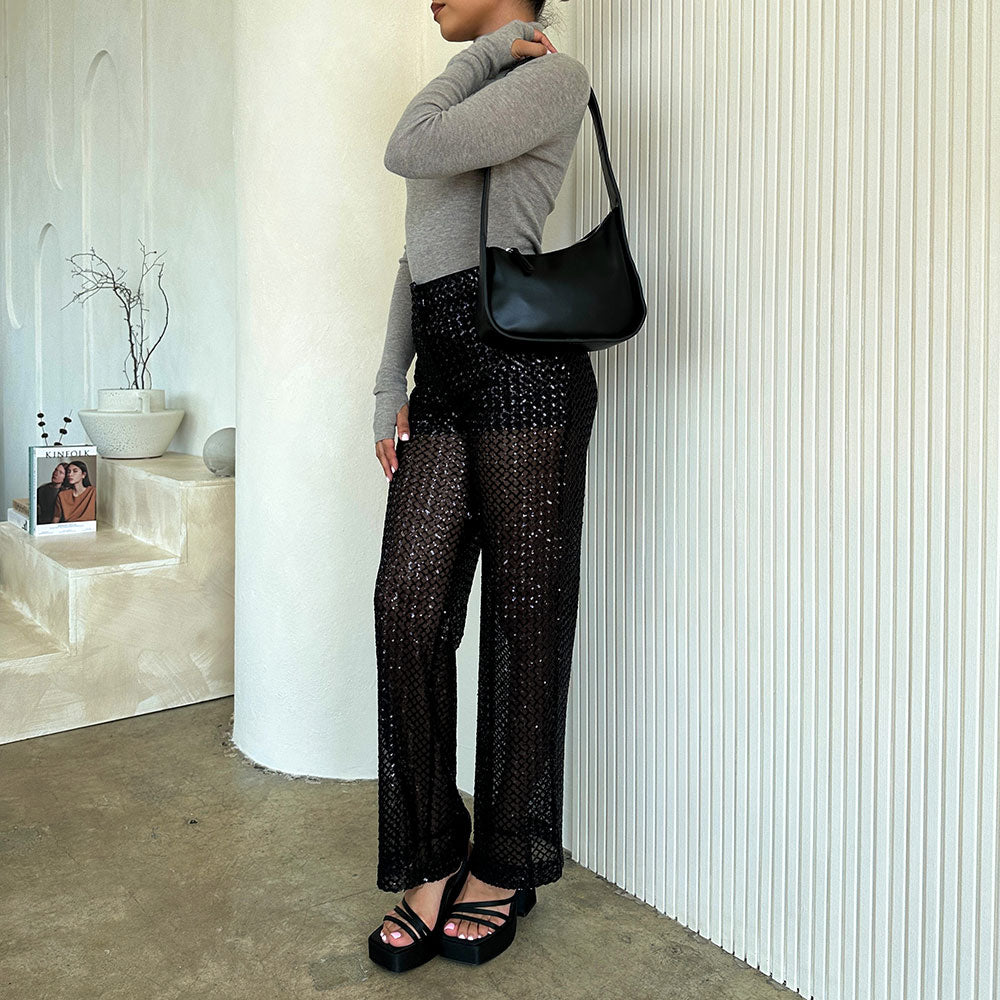 A model wearing a asymmetrical vegan leather structured shoulder bag against a white wall. 