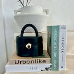 A still image of a small recycled vegan leather top handle bag with silver hardware with books and a vase.