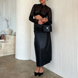 A model wearing a small recycled vegan leather top handle bag with silver hardware against a white wall. 