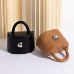 A still image of two recycled vegan leather top handle bag with silver hardware against a tan wall. 