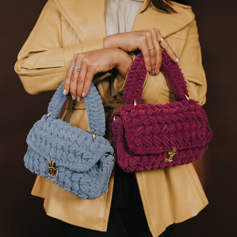 Model holding a sky knitted handbag and a plum knitted handbag with gold clasps. 