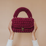 A model holding up a plum knitted crossbody handbag with gold clasp. 