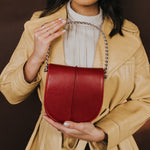 A model holding a red vegan leather crossbody handbag with a yellow jacket on. 
