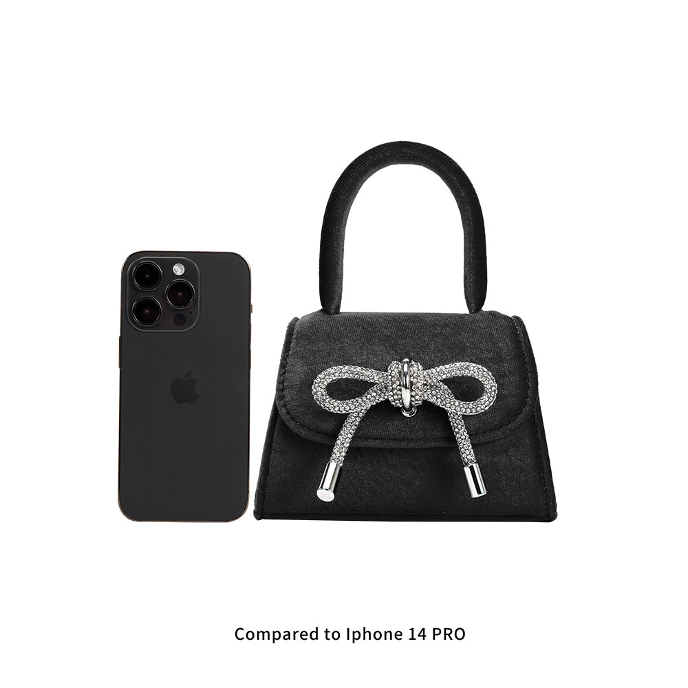An iphone 14 pro size comparison image for a mini velvet top handle bag with a silver encrusted bow.
