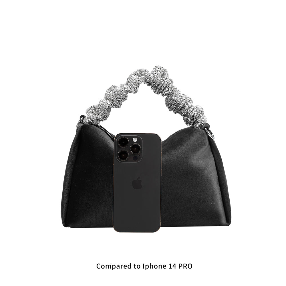An Iphone 14 pro size comparison image for a velvet top handle bag with a silver encrusted handle. 