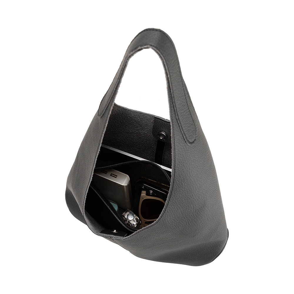 An inside view image of a large recycled vegan leather shoulder bag with a laptop, phone, and charger inside. 