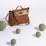 A still image of a medium saddle vegan leather crossbody bag against a white background with green ball props.