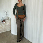 A model wearing a small crescent vegan leather crossbody bag against a white wall. 
