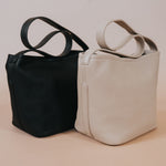 A still image of two recycled vegan leather shoulder bags with adjustable straps against a tan wall. 