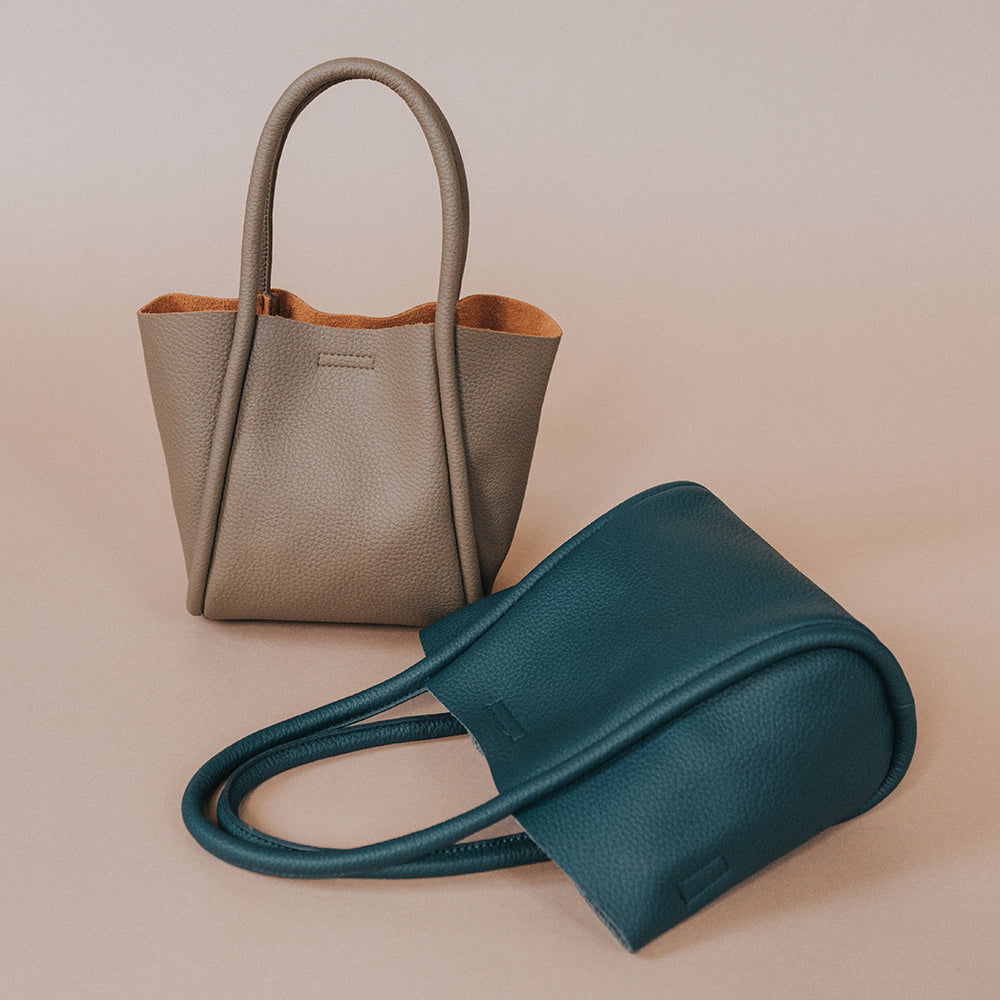 A still image of two small recycled vegan leather tote bags against a brown wall. 