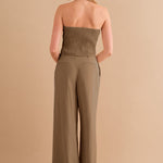 A backside view of a model wearing a two piece strapless top and pant set against a tan wall. 