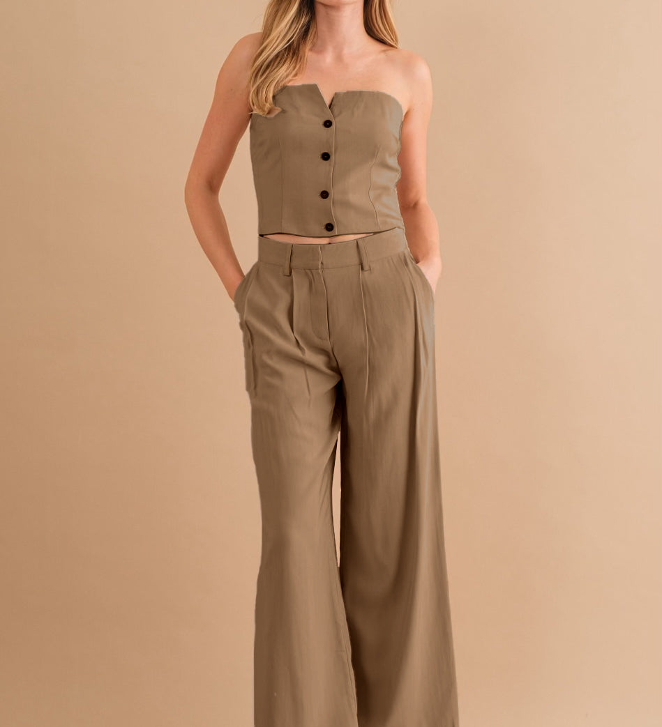 A model wearing a two piece strapless top and pant set against a tan wall. 