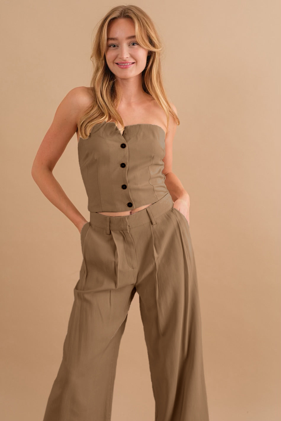 A model wearing a two piece strapless top and pant set against a tan wall .
