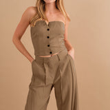 A model wearing a two piece strapless top and pant set against a tan wall .