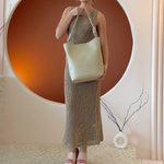 A model wearing a large vegan leather tote bag with a knotted handle.