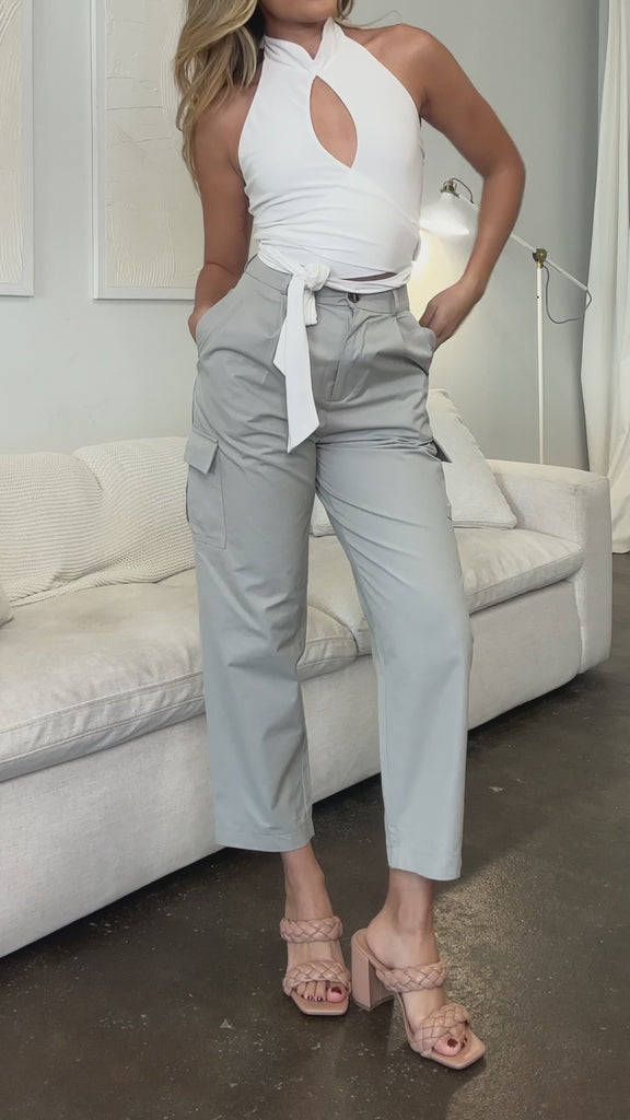 Video of a model wearing a beige high rise cargo pant with a white couch in the background. 