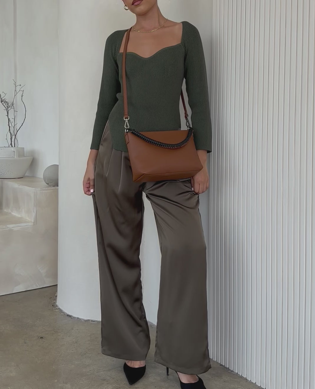Video of a model wearing a small vegan leather crossbody handbag against a white wall.