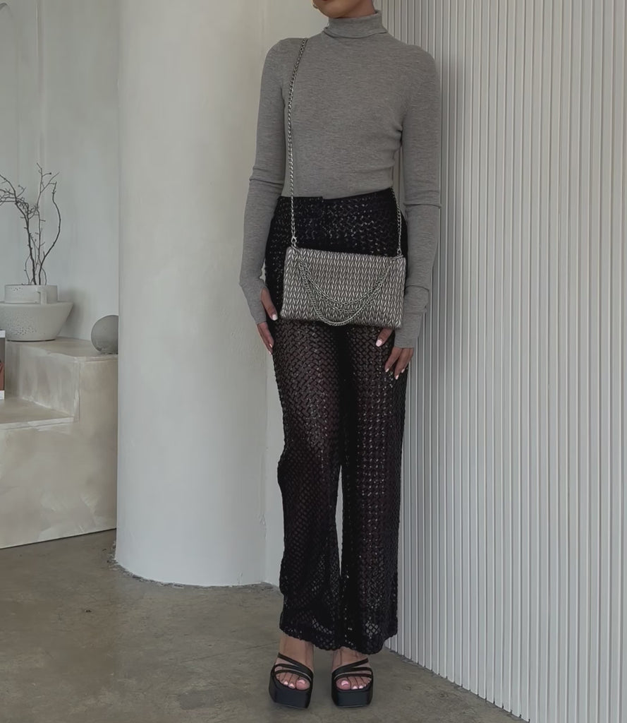 Video of a model wearing a small quilted pattern crossbody clutch against a white wall. 