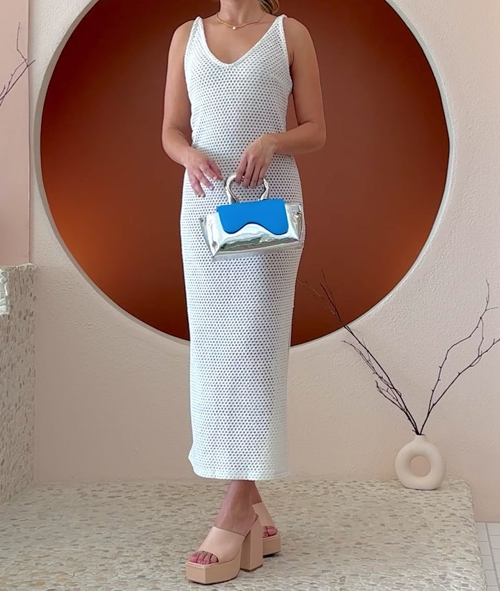 Video of a model wearing a small vegan leather top handle bag with a wavy front flap closure.