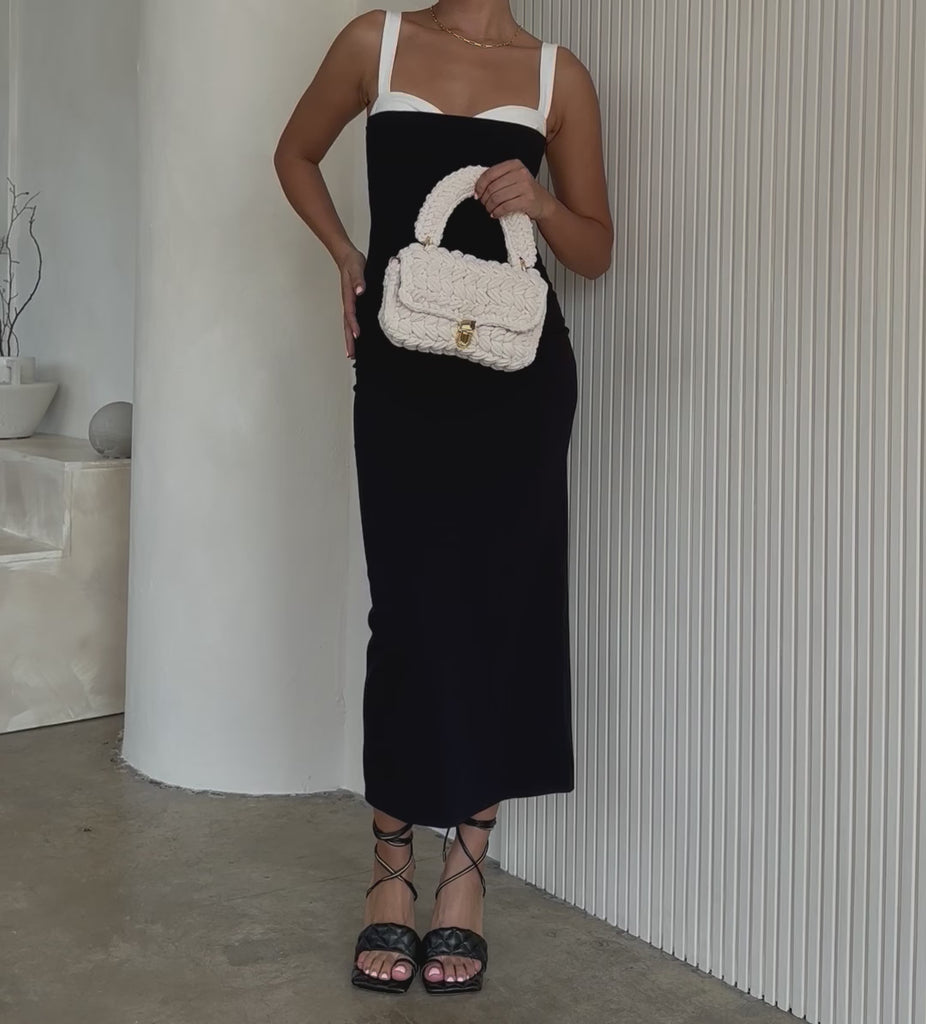 Video of a model holding a a ivory knitted handbag with gold clasps against a white wall. 