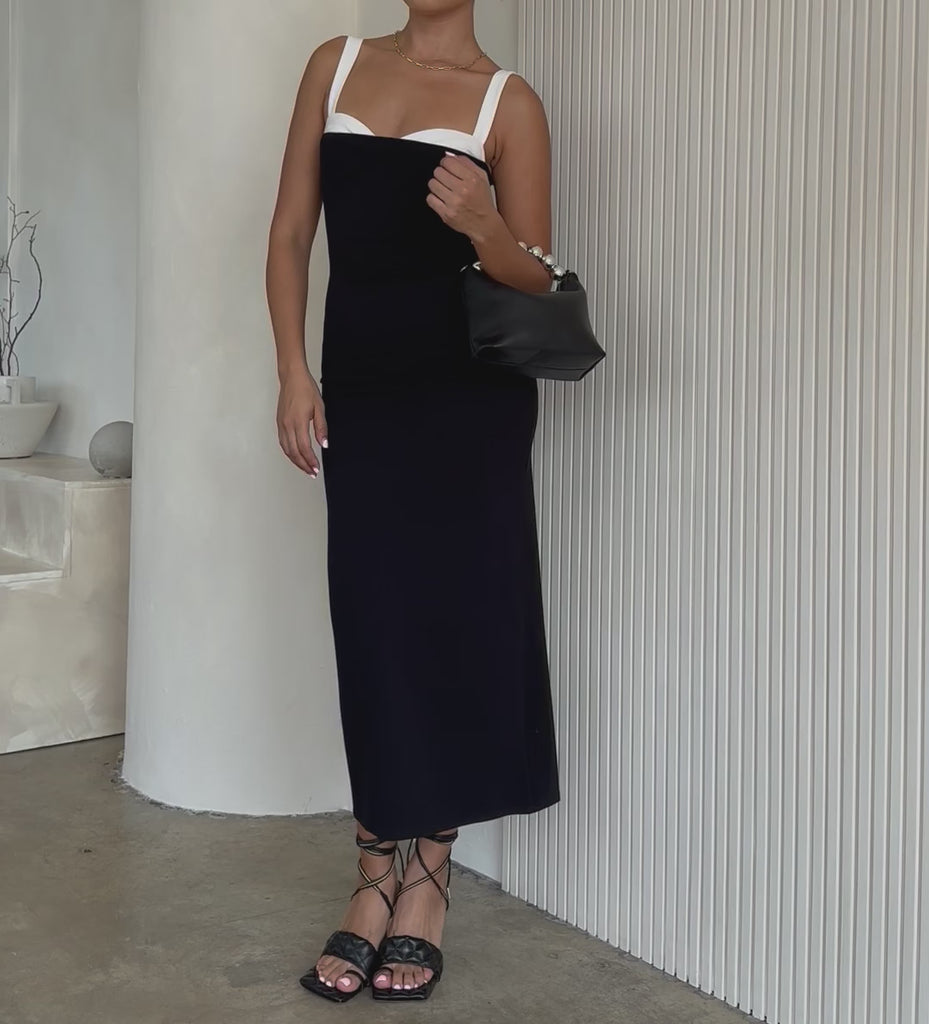 Video of a model holding a small recycled vegan leather crossbody bag against a white wall. 