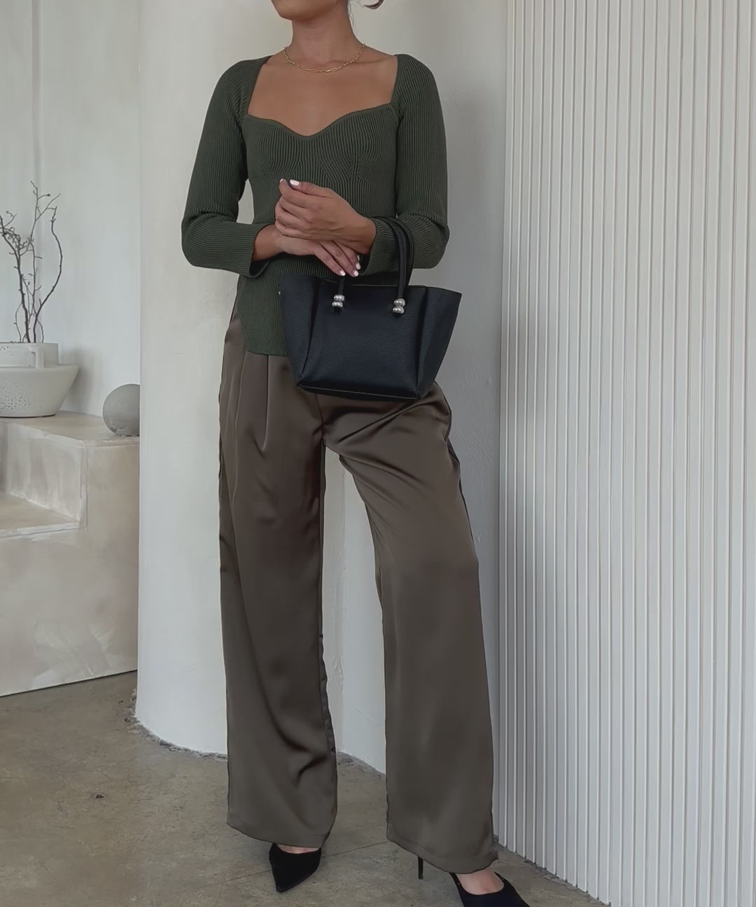 Video of a model wearing a recycled vegan leather top handle bag against a white wall. 