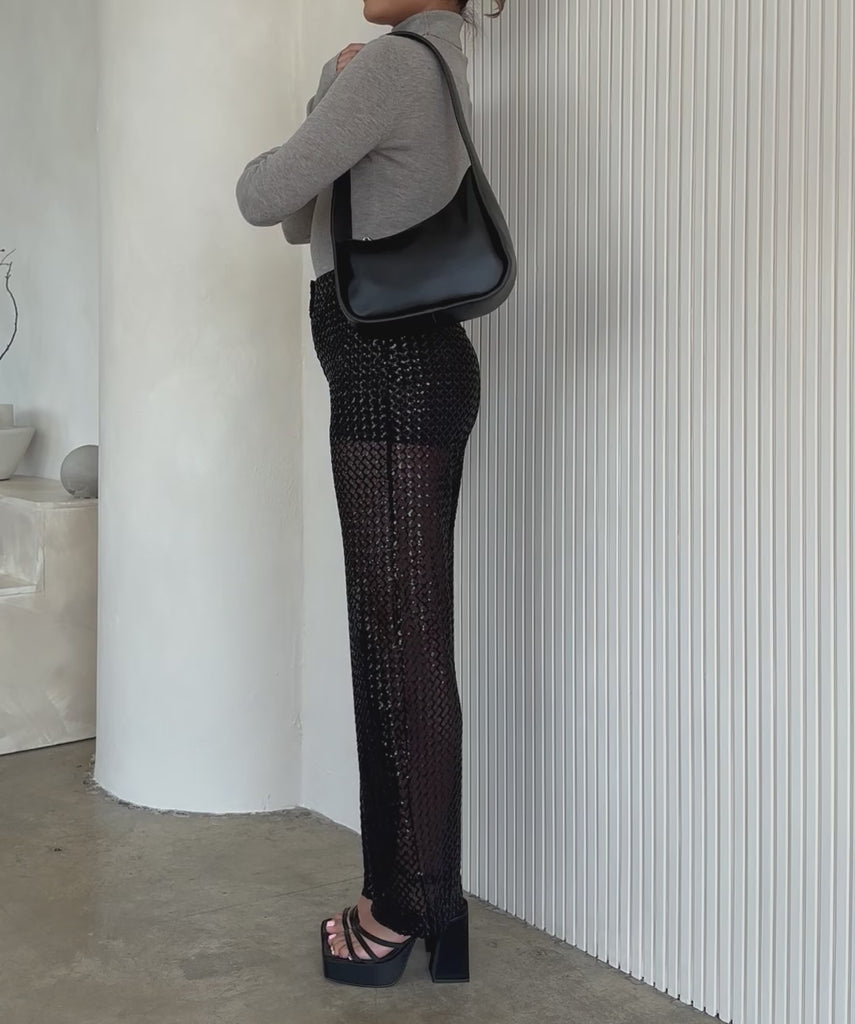 Video of a model wearing a asymmetrical vegan leather structured shoulder bag against a white wall. 