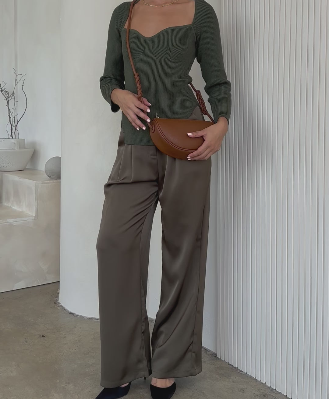 Video of a model wearing a small crescent shaped vegan leather crossbody bag against a white wall 