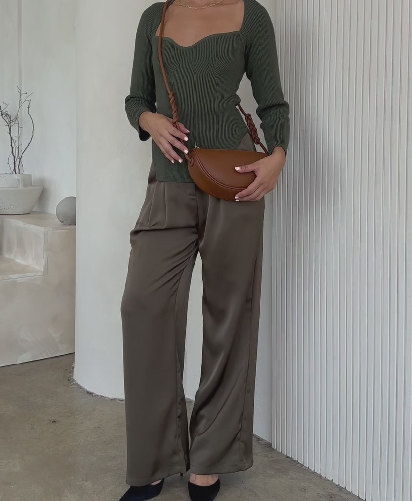 Video of a model wearing a small crescent shaped vegan leather crossbody bag against a white wall 
