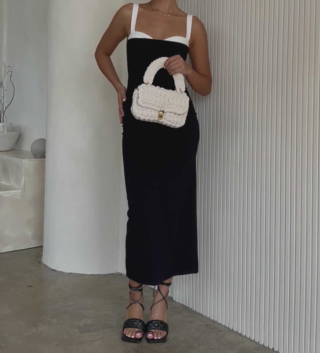 Video of a model holding a white knitted crossbody handbag with gold clasps against a white wall.